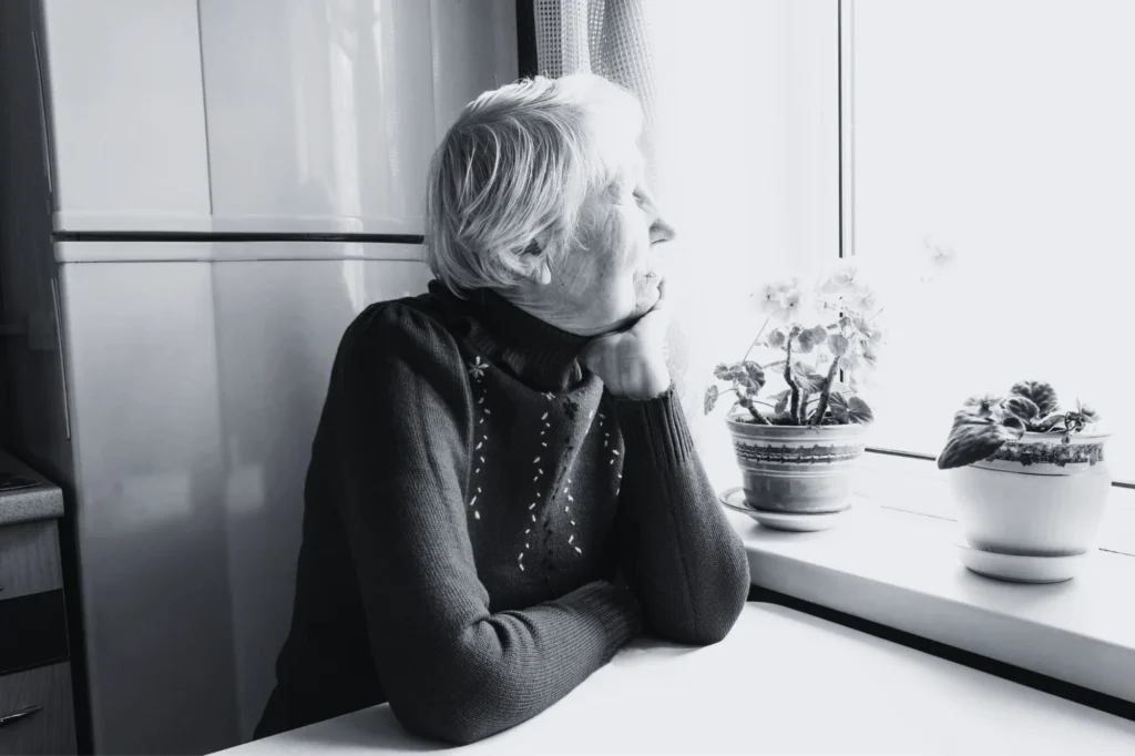 Mujer mayor sola sentada en una mesa y mirando por la ventana